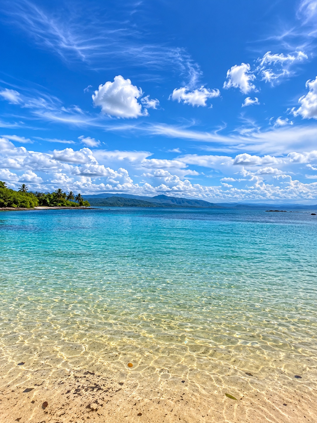 Crystal-clear beach with mountains and a blue sky